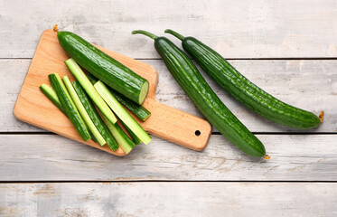 Board with cut and whole cucumbers on light wooden background