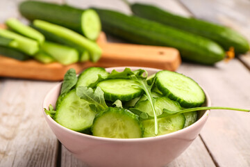 Bowl with fresh cut cucumber on light wooden background, closeup