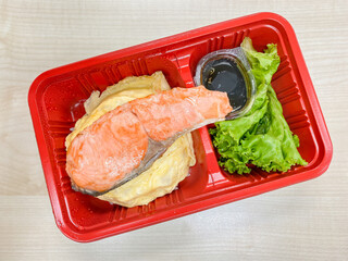 Salmon grilled with salad in the food container on the table