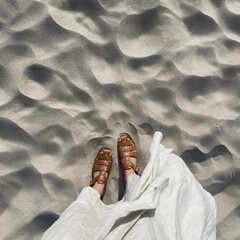 Women feet on desert beach sand. Aesthetic summer vacation background. Woman in white dress and...