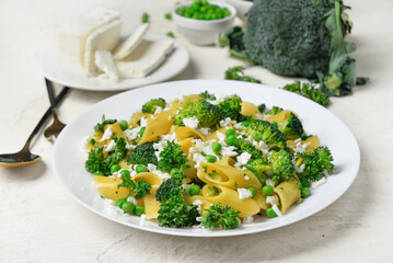 Plate with tasty penne pasta and broccoli on light grunge background