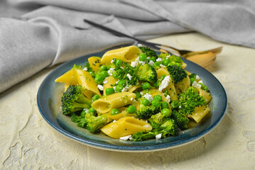 Plate with tasty penne pasta and broccoli on light grunge background
