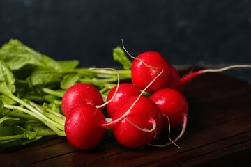 Wooden board of ripe radish with green leaves on dark background