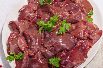 Raw chicken liver on stone background. Fresh ingredients ready for cooking, parsley, red pepper