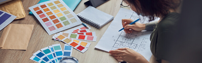 Close up shot of working process of interior designer making notes on a blueprint, selecting color samples, sitting at the table in her office
