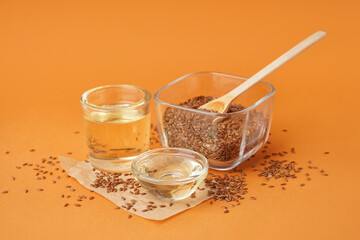 Glass with flax oil and bowl of seeds on orange background