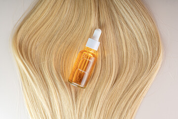 A smoothing strand of blonde hair and a hair care serum lying on a beige background. Serum or oil close up