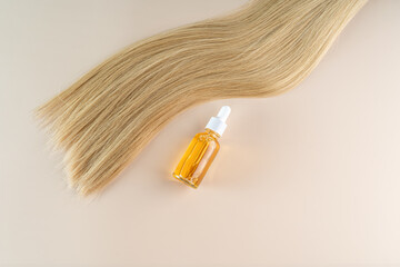 A smoothing strand of blonde hair and a hair care serum lying on a beige background. Serum or oil...