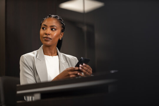 A beautiful black businesswoman is using a smartphone while waiting for a late meeting in the conference room.