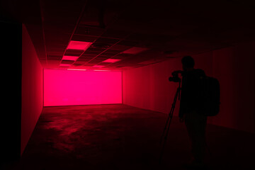 Silhouette of a person taking photo in a hall of pink neon light background	