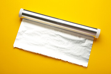 Roll of aluminum foil on yellow background.