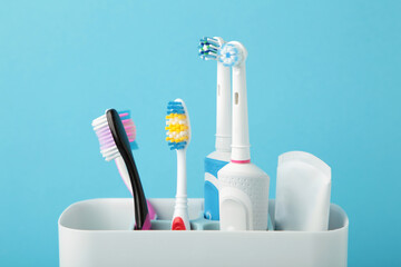 Holder with modern electric toothbrushes and manual toothbrushes on blue background