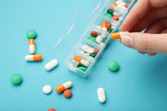 Female hand sorting pills in pillbox on blue background