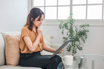 タブレットを見て考える・困る・悩むアジア人女性
