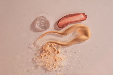 A sample of red lip gloss, foundation, powder and gel makeup base on a beige background.