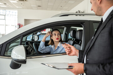 young woman standing near new modern car at the dealership and choosing the best auto with salesman