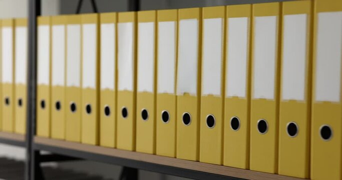 Yellow folders with documents are arranged in rows on shelves in office. Company business documentation