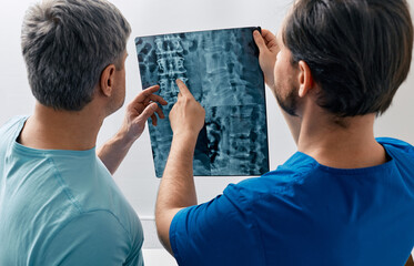 Manual therapist viewing X-ray of backbone with his male patient with spinal problem during medical...