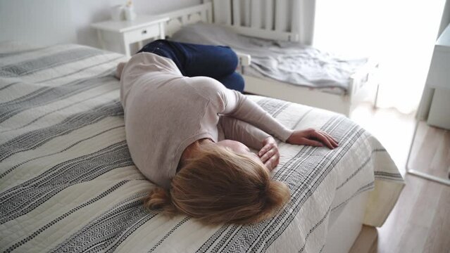 Mature woman curled lying on the bed at home. Depression, mental health, abuse problem