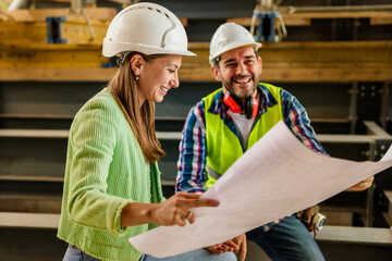 Two happy civil engineer and maintenance engineer in protective vests and helmets working on a...