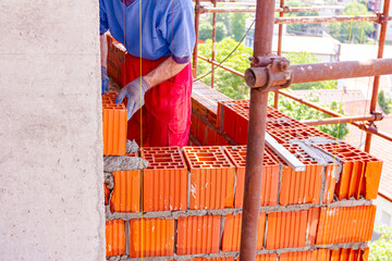 Worker is building wall with red blocks and mortar