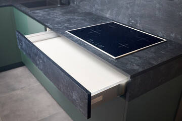 Induction cooker black tempered glass hob aspirating induction hob on marble stoneware countertop with horizontal sliding pull out drawer shelf storage in kitchen cupboard.