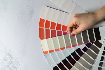 Fototapeta na wymiar Female hand holding open color palette guide catalog with colour swatches. Architect or home interior design concept. Choosing paint colors for a house, flat lay composition with copy space.