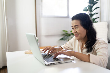 Fototapeta na wymiar Middle age Asian woman Work from home. senior woman smiling Beautiful mature asian woman on laptop with technology concept