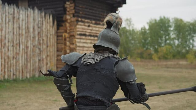 Knight with skull on helmet swings spear near burnt house