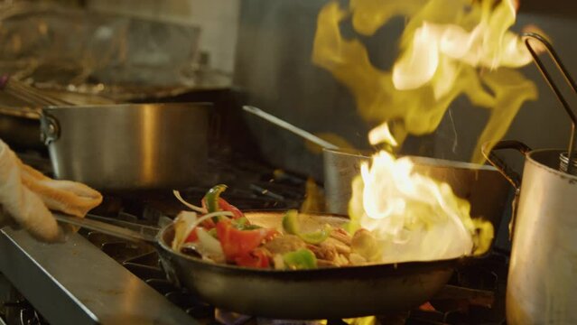 Vegetables cooking sizzle fire flame saute pan oil commercial kitchen tongs