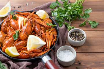 cooked crawfish in black saucepan with lemons and spices on wooden background