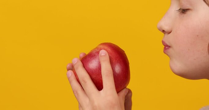 Pretty teen girl, child eat, bites a fresh red apple isolated on studio yellow background, healthy snack choices, wholesome food lifestyle concept, copy space