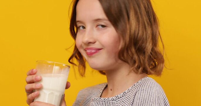 Pretty teen girl, child with a fresh glass of milk isolated on studio yellow background, strong bones, milk for growth, healthy lifestyle concept, copy space