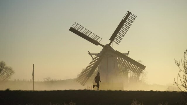 Man running on a levee in the foggy, Dutch countryside near a windmill.