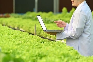 Geneticists, biologists, scientists holding laptop while working on research in industrial greenhouse