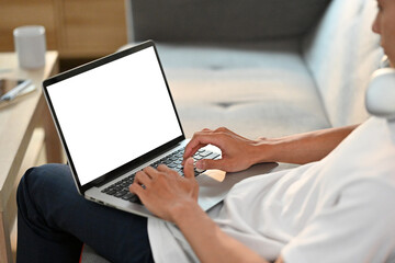 Close up view of casual man browsing internet on laptop, resting on couch in bright living room