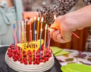 Happy birthday cake with colorful candles burning and many red wild strawberries