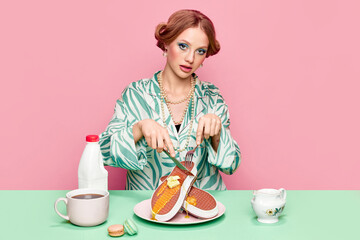 Pretty girl with makeup and hairdo cutting surreal sneakers waffles with honey and butter against...