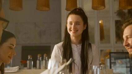 Guests watching menu, talking with female worker and making the order. Waitress serves group of friends in restaurant. Celebrating anniversary, birthday dinner. Concept of public eating. Portrait view