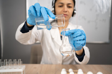 Chemistry teacher shows a chemical experiment with liquids in flasks has an online lesson uses a wireless headset