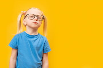 Portrait of little blonde girl with glasses and looks pensively into the distance. Preschooler on yellow background. Copy space