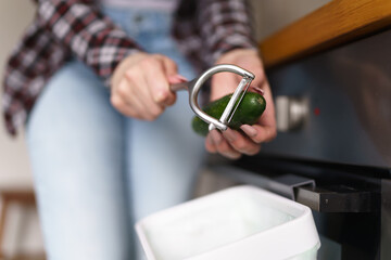 Female person peeling off a cucumber and recycling peels in a compost bin at home