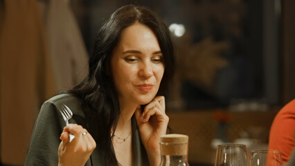 Close up shot of woman eating and enjoying delicious food, talking to friends in modern gastro cafe. She celebrates birthday, has family dinner, spends evening in restaurant. Concept of public eating.