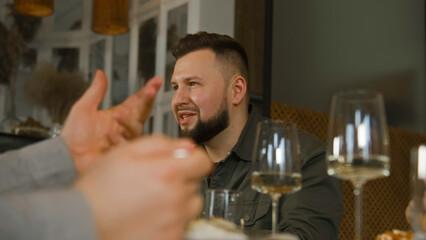 Caucasian man sits in modern gastro cafe, eats delicious dish and talks to friends. Group of people celebrate birthday, have family dinner, spend weekend together in restaurant. Public eating concept.