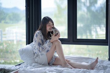 Portrait of young Asia woman hugging her cute pet prairie dog on white bed at home in holiday. Human and lovely animal,   Adorable domestic pet concept.