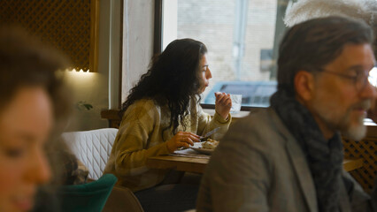 Young woman sits at the table in modern cafe, eats delicious food, works on freelance in laptop. Female freelancer has dinner in restaurant, talks to waiter. Concept of remote work and public catering