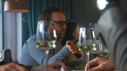 Caucasian man talks to friends on meeting in modern gastro cafe. Family celebrate birthday party together in restaurant. Served table with tasty dishes and glasses of wine. Concept of public catering.