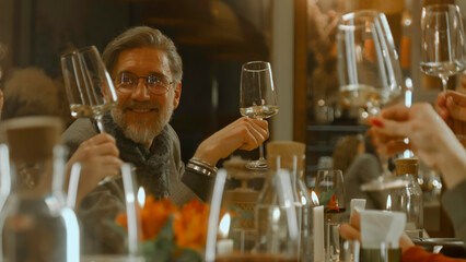 Close up shot of waiter pouring red wine from the bottle into the glass in restaurant. People clink glasses, celebrate birthday, spend weekend evening in modern gastro cafe. Public catering concept.