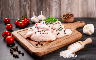 Raw meat. Chicken wings lie on a wooden board with vegetables and spices on a black background.