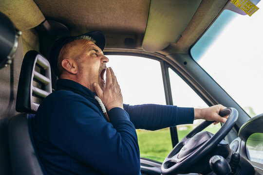 Mature truck diver feeling tired and yawning during the ride.